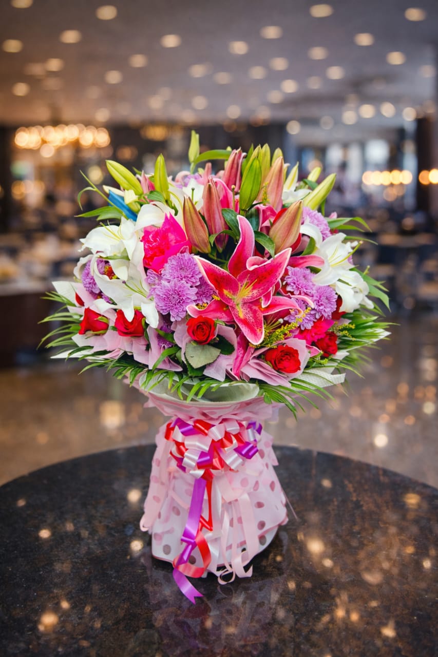 This is a vibrant mixed flower bouquet featuring 'Stargazer' lilies, roses, and carnations.